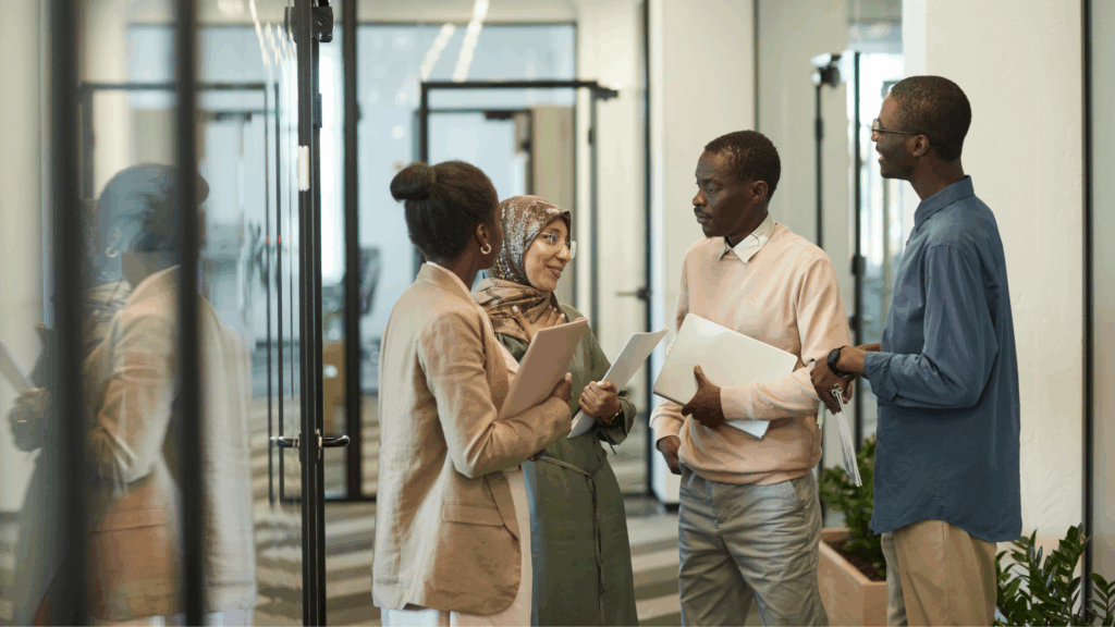 four business people in office hallway discussing work