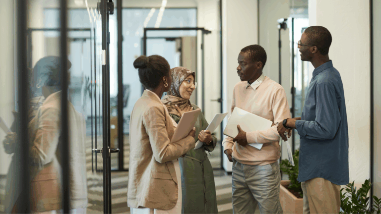 four business people in office hallway discussing work
