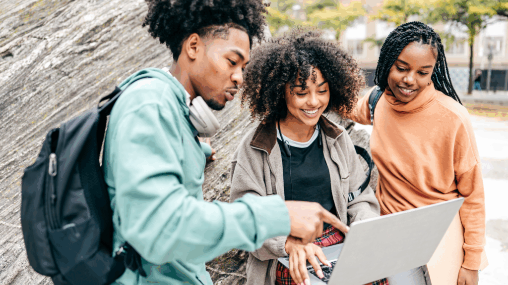three students outdoors looking at laptop reviewing legal tech information
