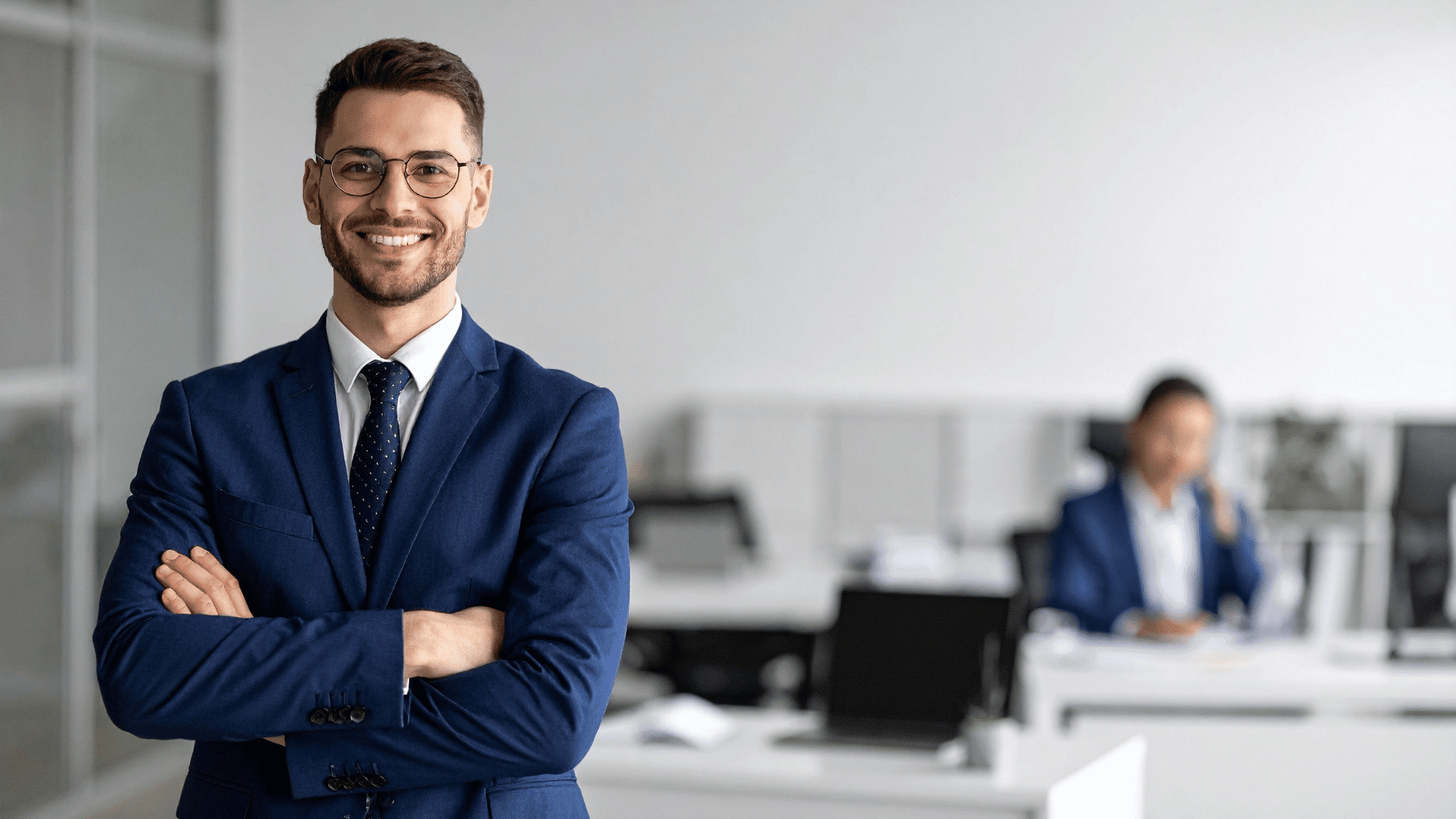 Young male adult business professional  wearing a suit and smiling in career office setting.