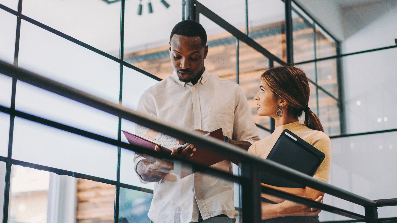 brunette woman and dark haired man in business casual clothing looking at portfolios