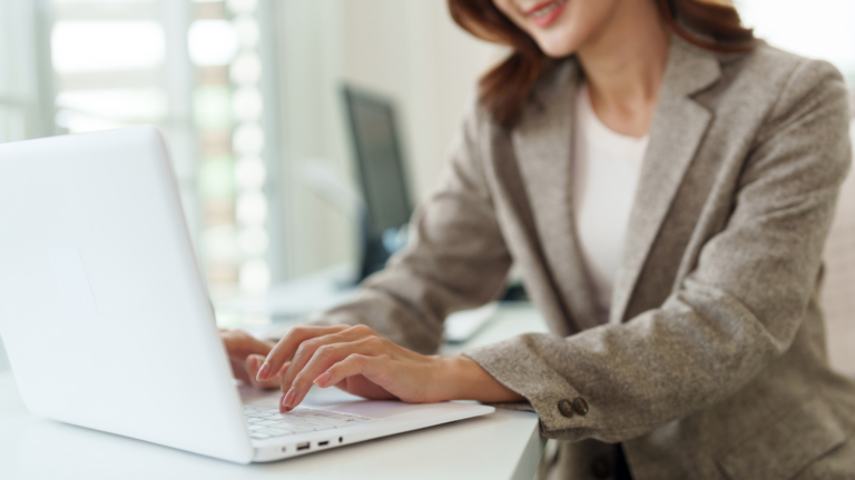 Woman in blazer typing on white laptop in office setting