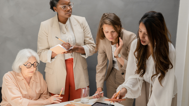 Four business women working in office pouring over documents on table and taking notes