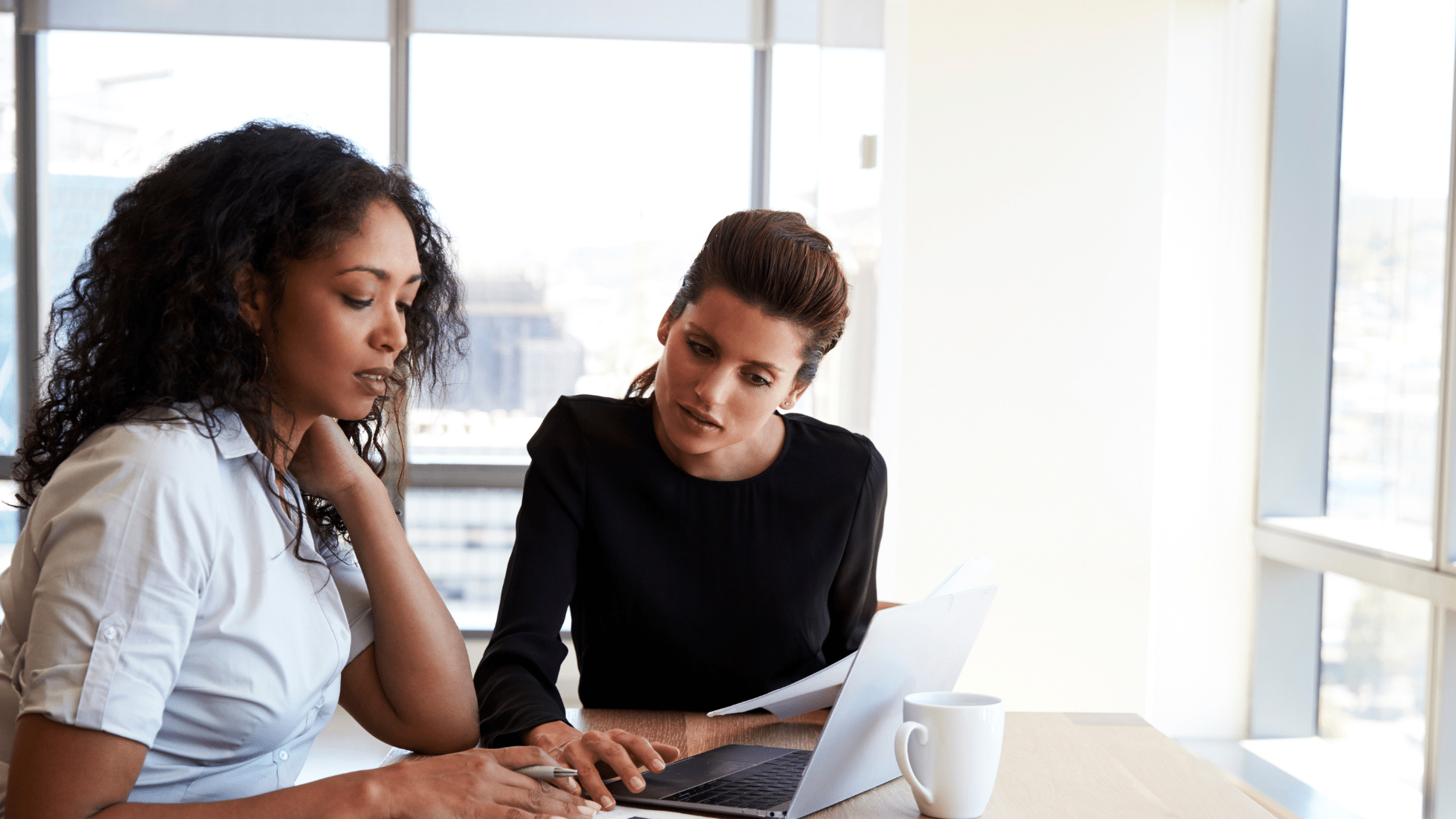 Two women at desk looking over documents, one woman looking distressed the other trying to sooth her