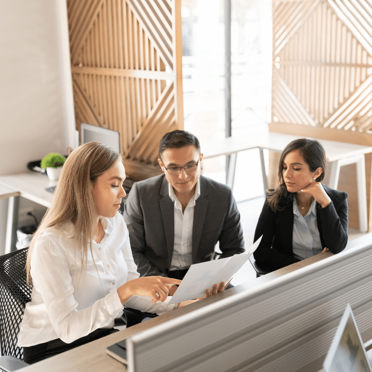 Three attorneys looking over documents and a computer in a bright airy office setting