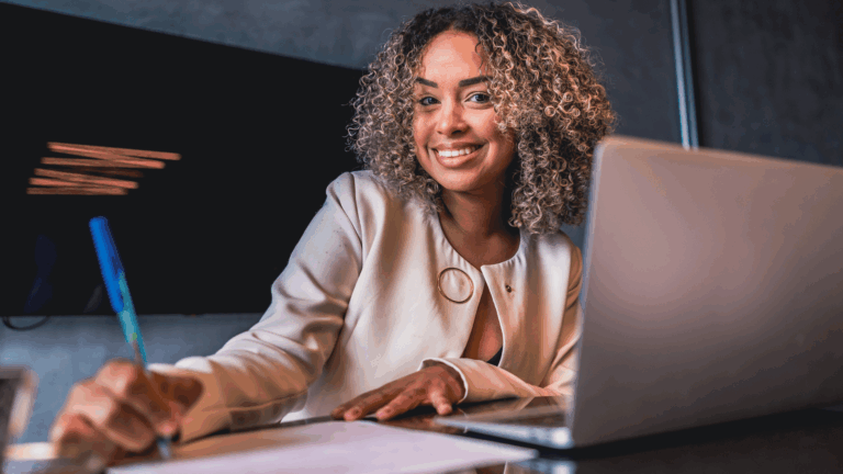 Young professional woman at desk working on laptop and taking notes